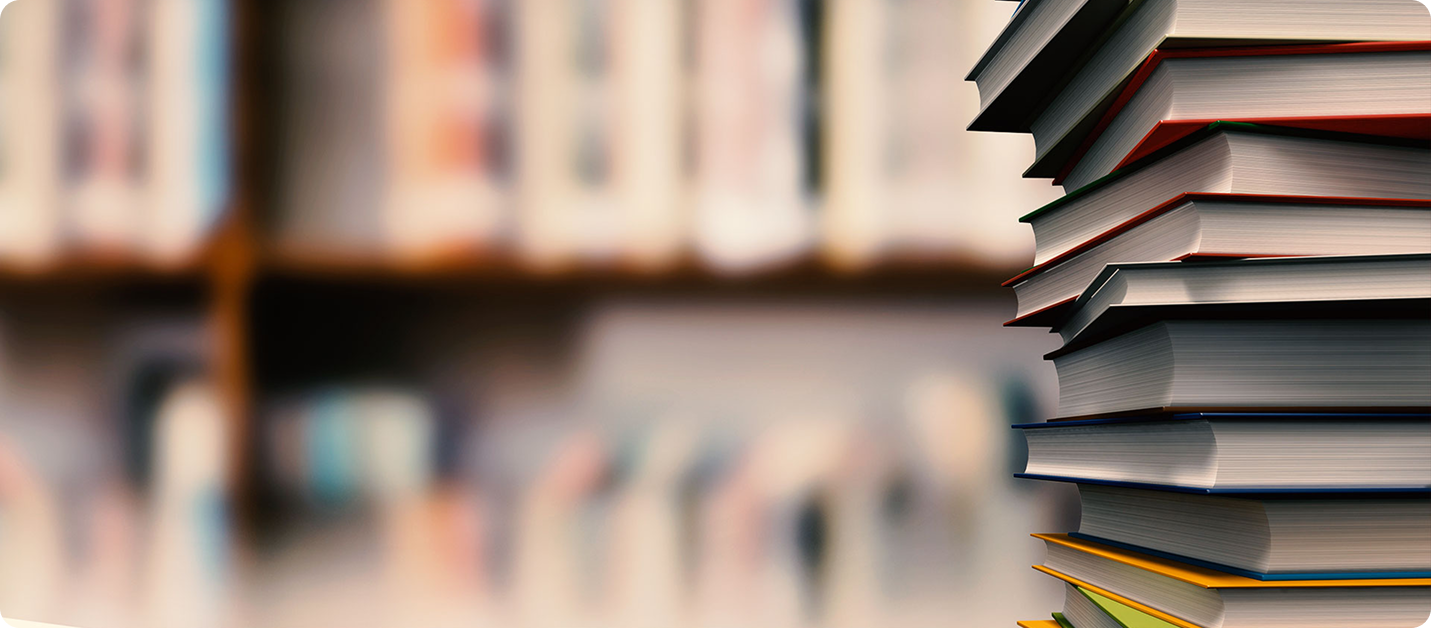 Tall stack of hardcover books standing next to a blurred library bookshelf scene