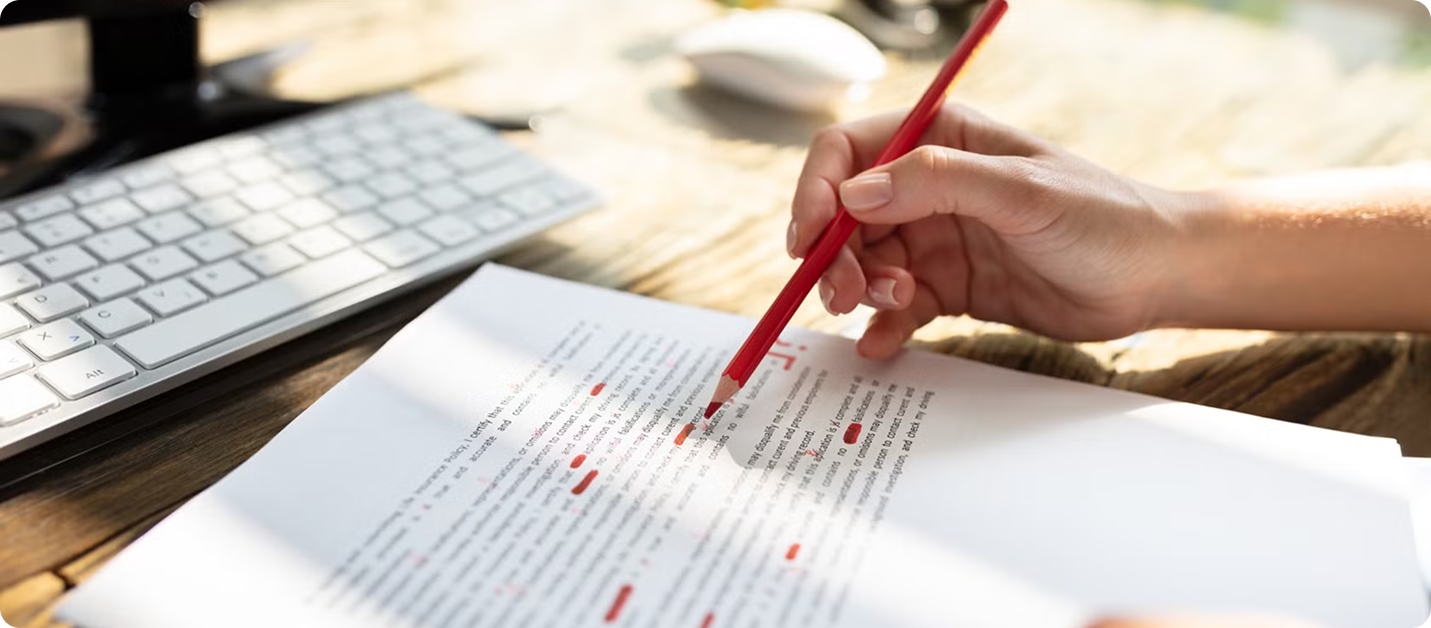 Hand holding red pencil marking corrections on printed document