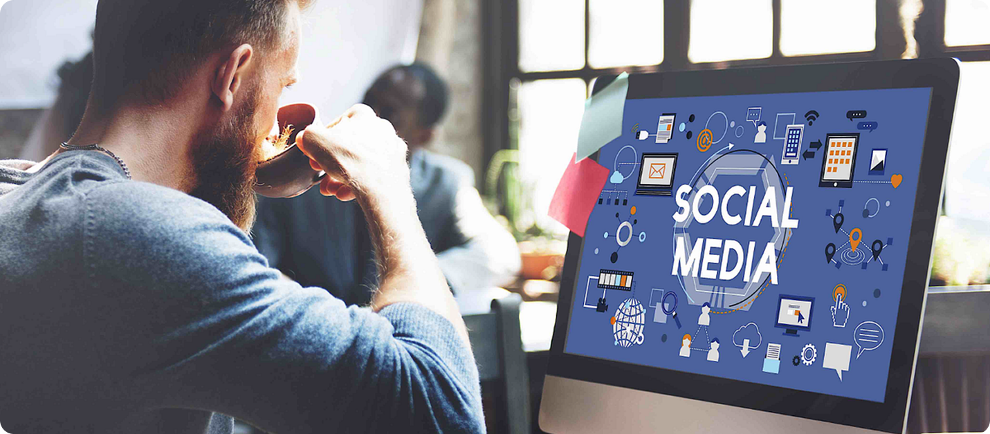 Man drinking coffee looking at laptop screen showing social media icons